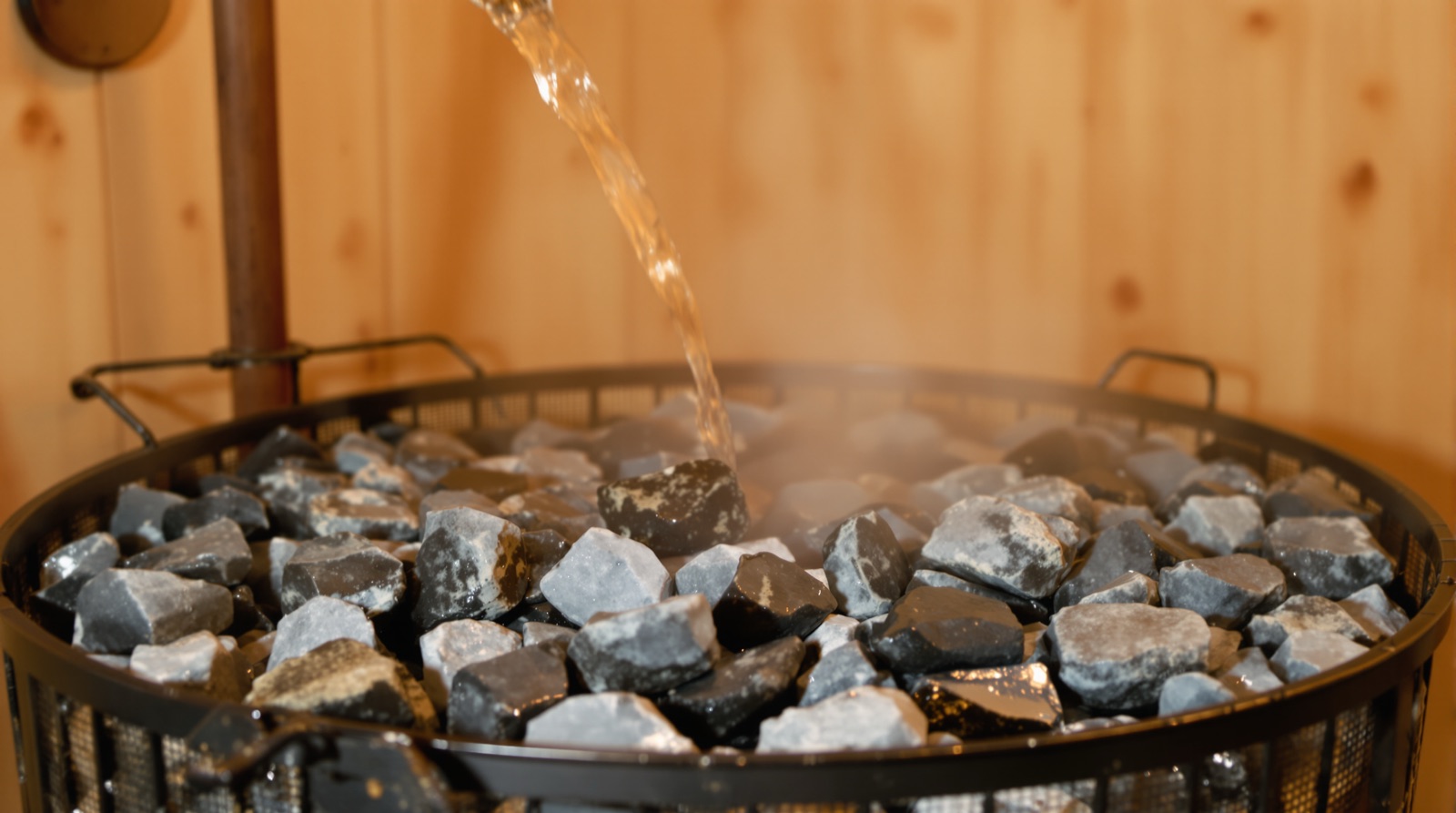 Sauna finlandesa: agua cayendo sobre las piedras calientes de la estufa